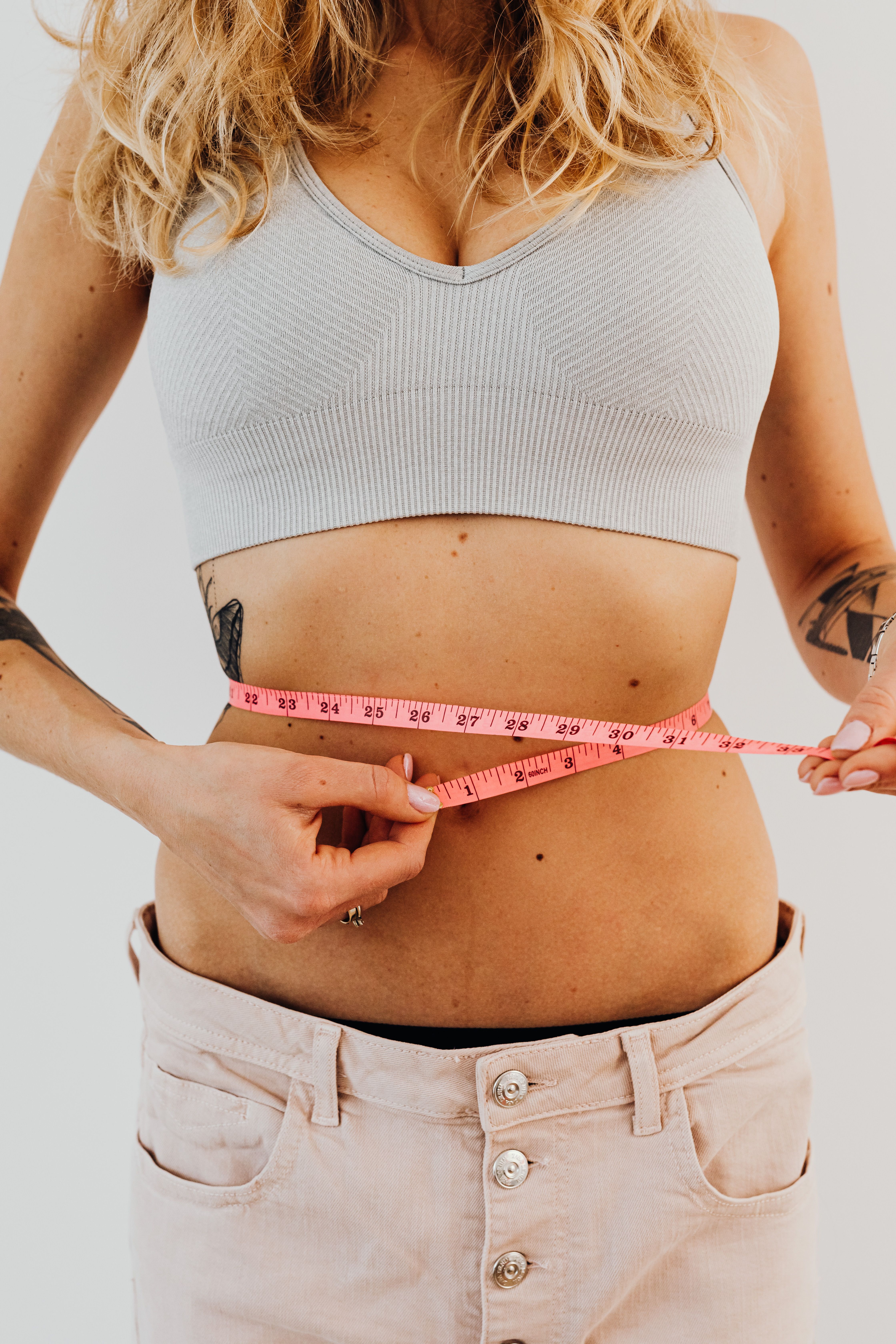 Woman checking her waistline with a pink measuring tape